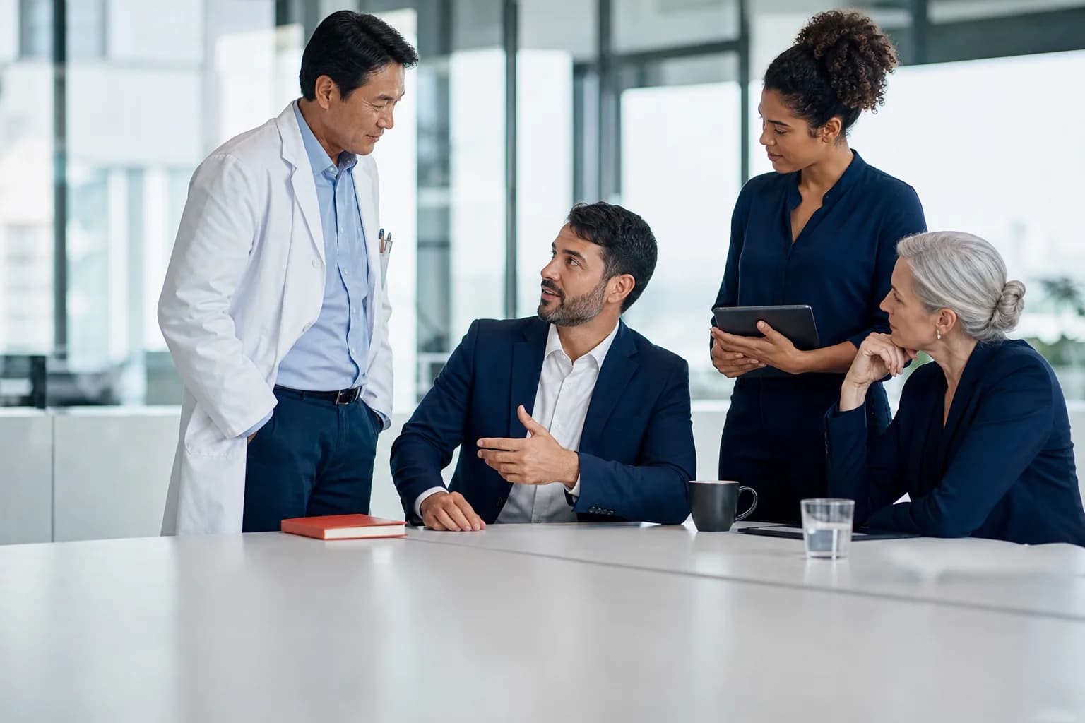 A doctor and three business colleagues talk around a table in a bright meeting room